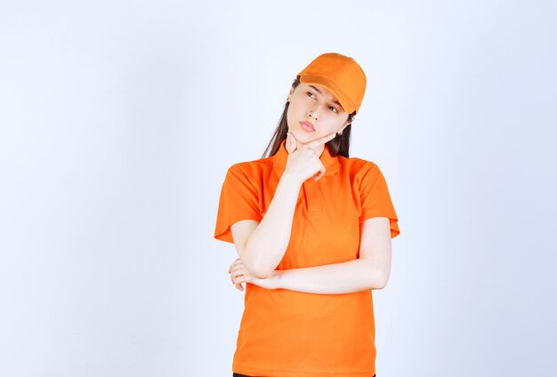 オレンジ色のドレスコードを身に着けている女性のサービスエージェントは、思慮深く見えます。