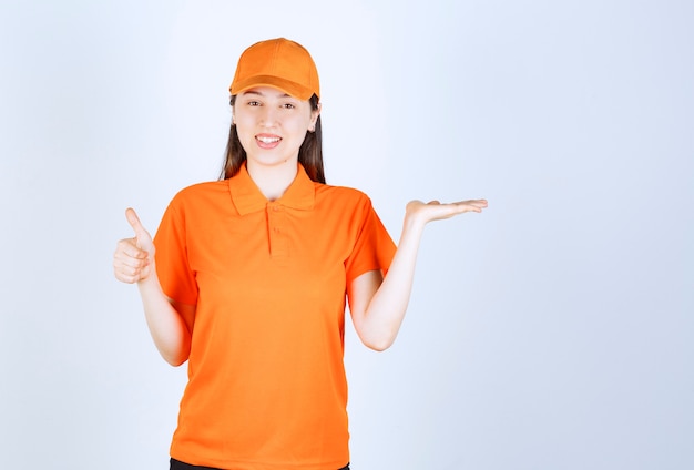 オレンジ色のドレスコードを身に着けて、肯定的な手のサインを示す女性のサービスエージェント