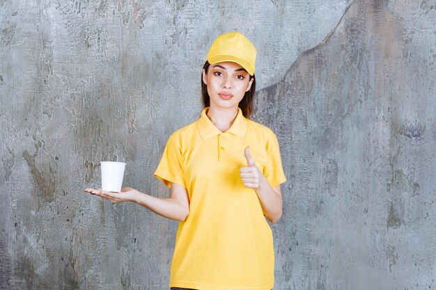 プラスチック製のコップを保持し、肯定的な手のサインを示す黄色の制服を着た女性サービスエージェント。