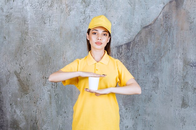 Female service agent in yellow uniform holding a plastic cup.