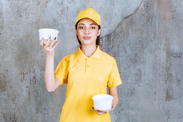 Female service agent in yellow uniform holding two plastic takeaway bowles in both hands