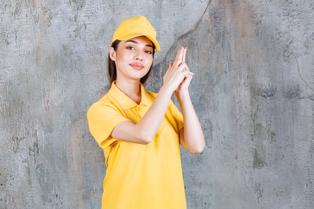 Женский служебный агент в желтой форме, стоящий на бетонной стене и держащий знак ручного пистолета.