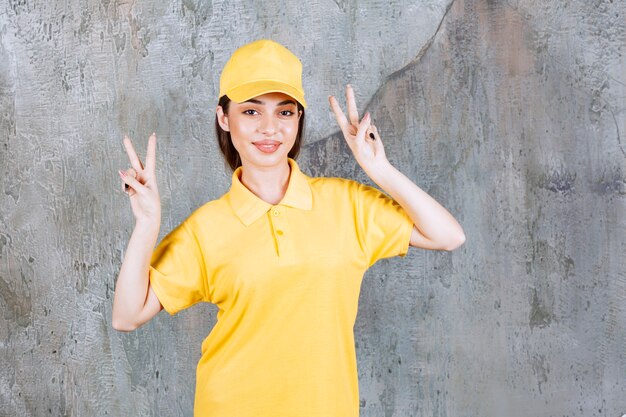 Female service agent in yellow uniform standing on concrete wall and sending peace.