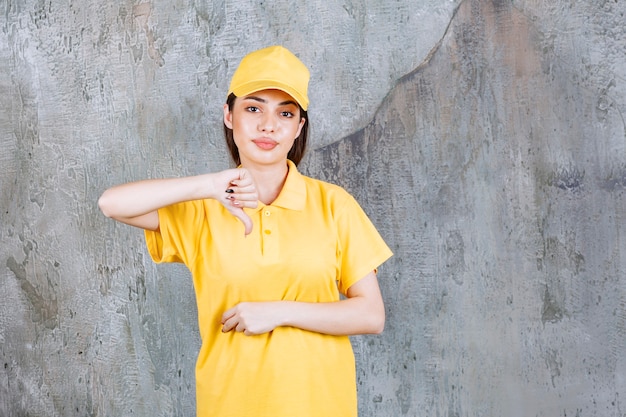 Free photo female service agent in yellow uniform standing on concrete wall showing thumb down.