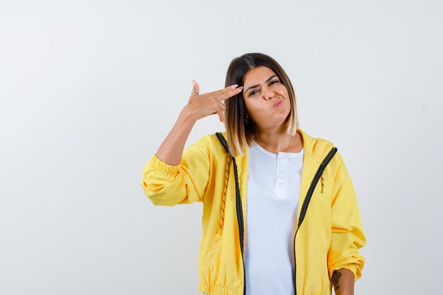 Female shooting herself with hand gun in t-shirt, jacket and looking hesitant , front view.