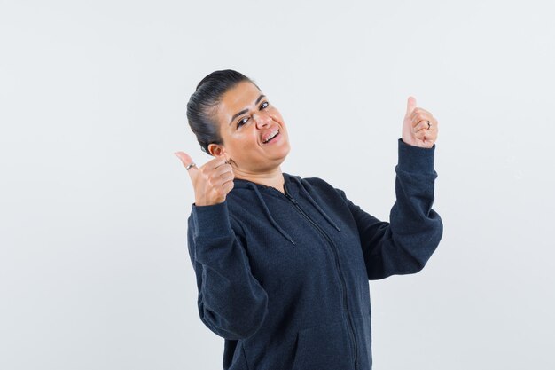 Female showing double thumbs up in hoodie and looking merry , front view.