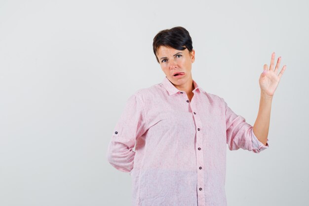 Female showing ok gesture, sticking out tongue in pink shirt front view.