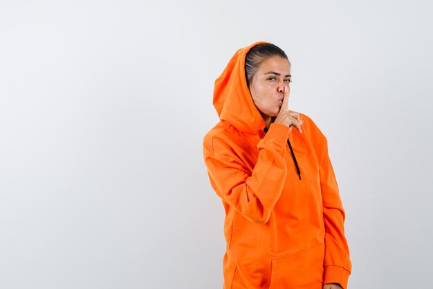 Female showing silence gesture in orange hoodie and looking charming