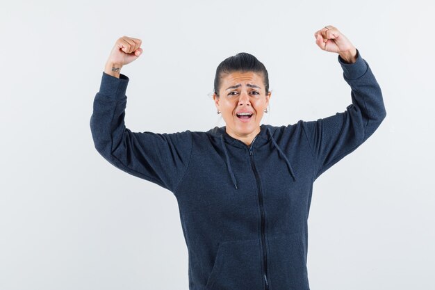 Female showing winner gesture in hoodie and looking blissful. front view.