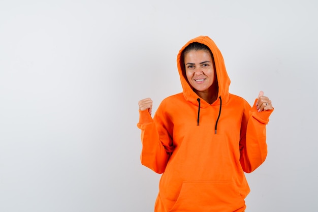 Female showing winner gesture in orange hoodie and looking lucky