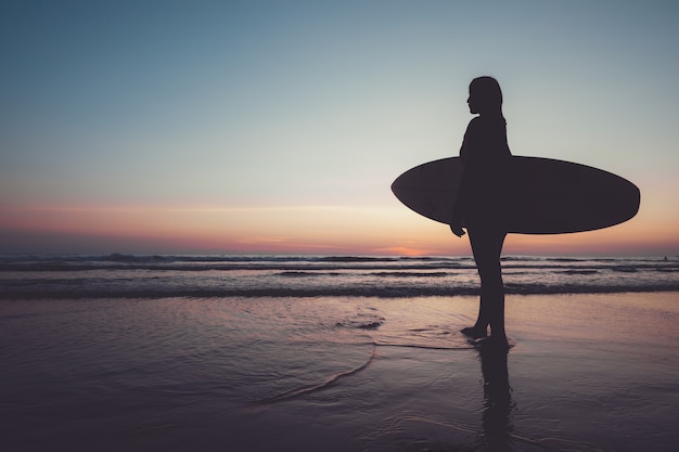 Female silhouette with surfboard on the beach at sunset