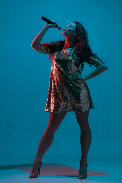 Female singer portrait isolated on blue studio wall in neon light