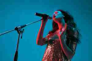 Foto gratuita ritratto di cantante femminile isolato sulla parete blu dello studio in luce al neon