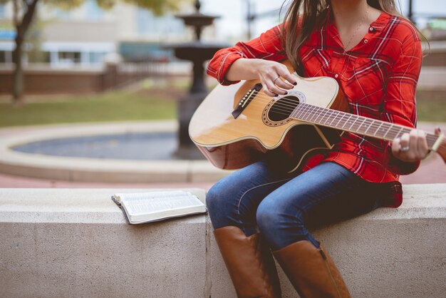 Женщина сидит возле книги во время игры на гитаре с размытым фоном