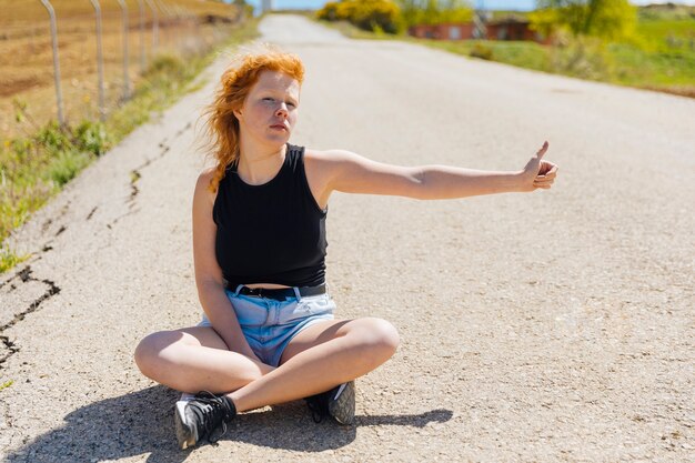 Женщина сидит на пустой дороге автостопом