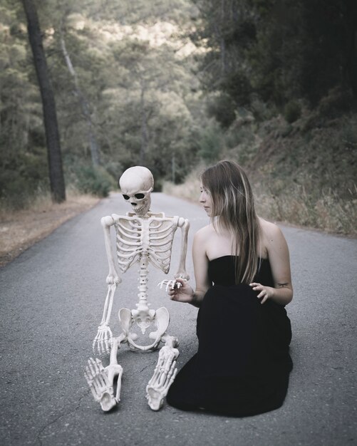 Female sitting on road and looking at artificial skeleton of man