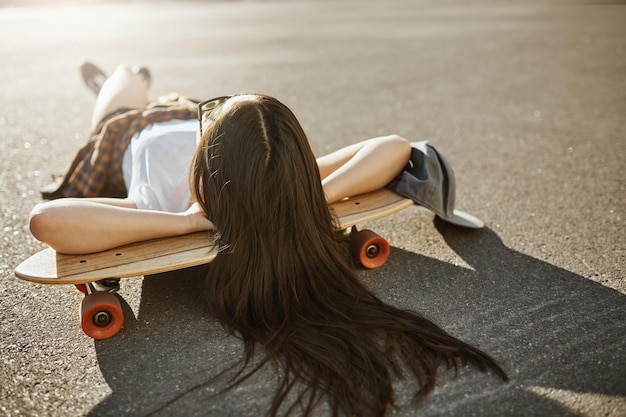 Female skateboarder laying on her lonboard on a sunny day relaxing