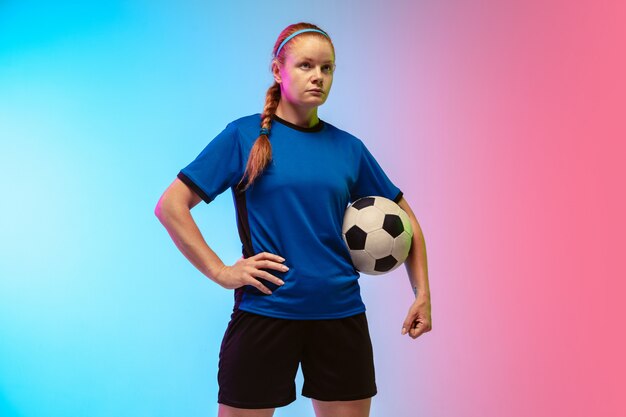 Female soccer, football player training in action isolated on gradient studio background in neon light