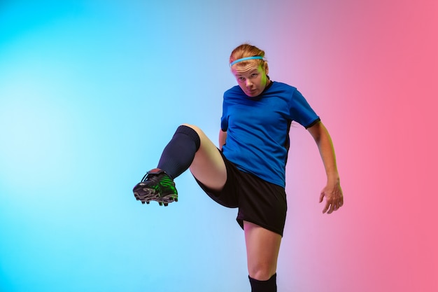 Female soccer, football player training in action isolated on gradient studio background in neon light