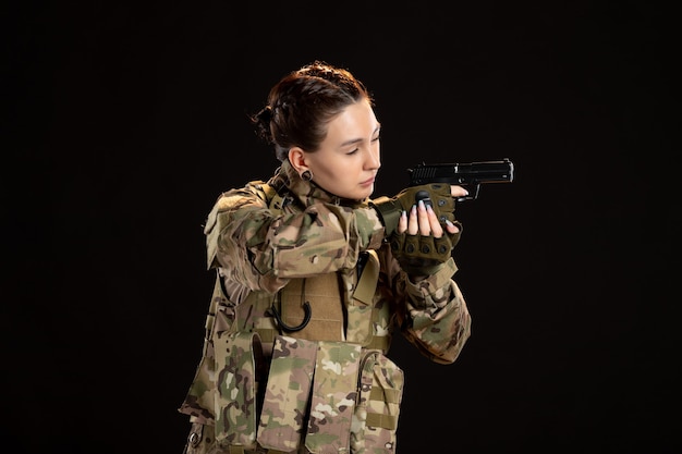 Женщина-солдат в камуфляже целится из пистолета на черной стене