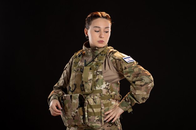 Female soldier in camouflage on the black wall