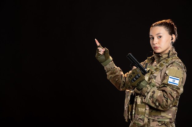 Женщина-солдат в камуфляже держит пистолет на черной стене