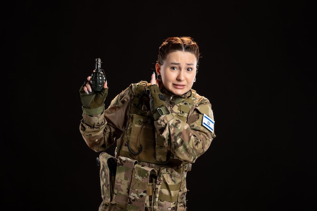 Female soldier in camouflage with grenade in her hands on black wall