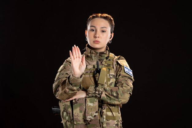 Бесплатное фото Женщина-солдат в камуфляже жестикулирует, чтобы остановиться на черной стене