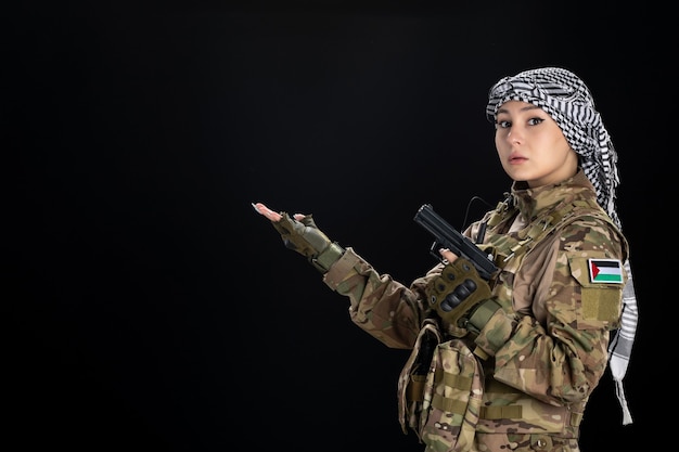 Female soldier in military uniform with gun on black wall