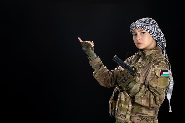 Женщина-солдат в военной форме с пистолетом на черной стене
