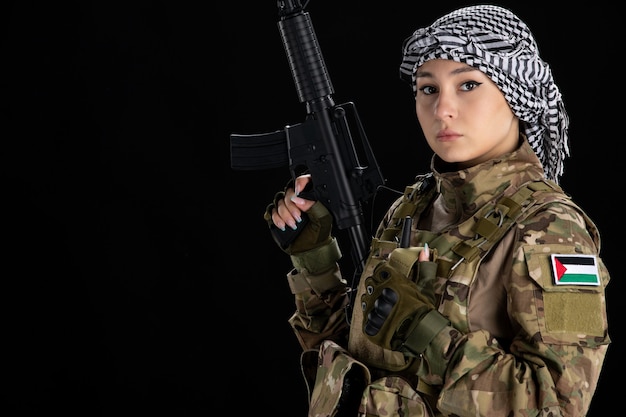 Female soldier in military uniform with machine gun black wall