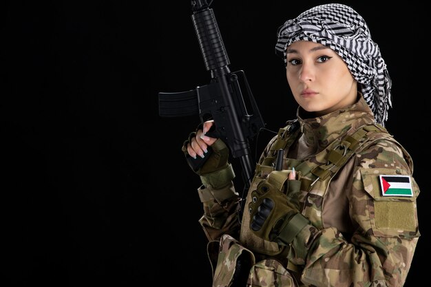 Female soldier in military uniform with machine gun black wall