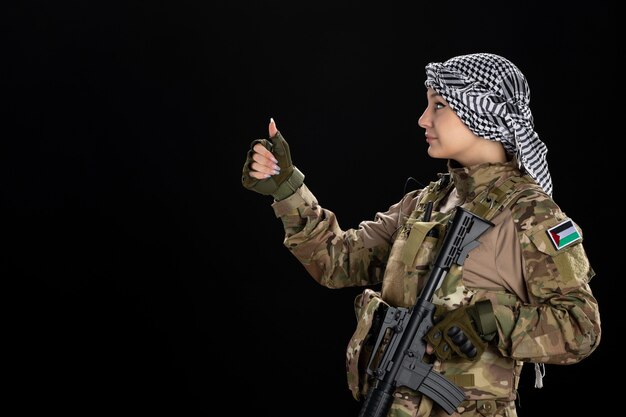 Female soldier in military uniform with rifle on the black wall