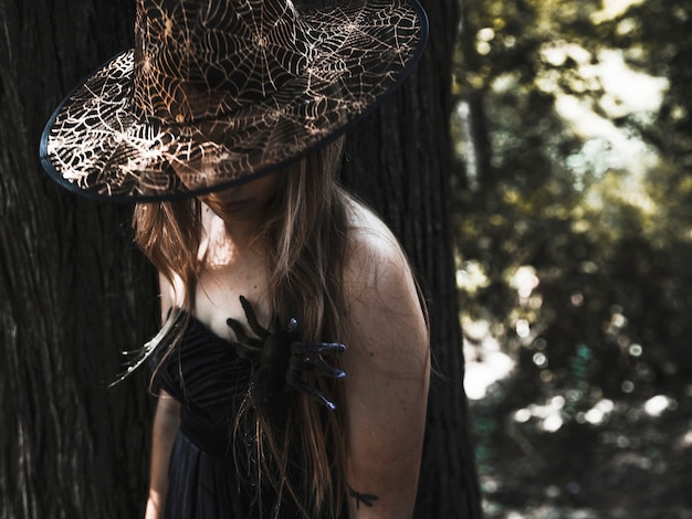 Female sorceress in hat and spider on chest in sunlit thicket