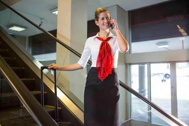 Female staff with luggage talking on mobile phone on escalator