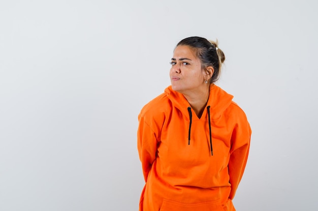 Female standing to hear clearly in orange hoodie and looking curious 