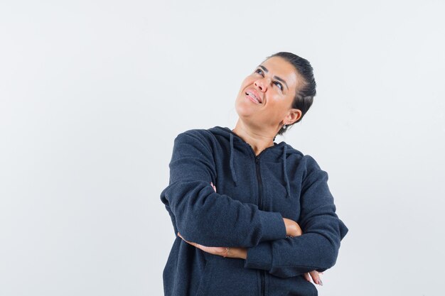 Free photo female standing with crossed arms in hoodie and looking dreamy , front view.