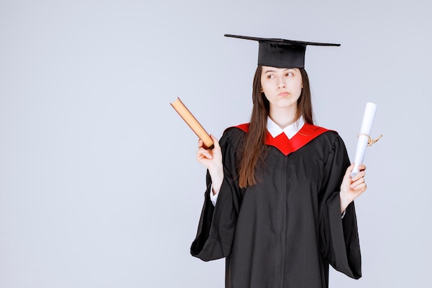 Female student in academic gown holding book and diploma. High quality photo