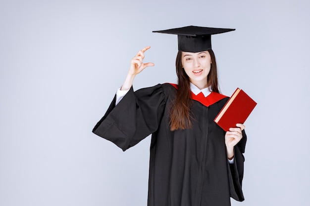 Studentessa in abito accademico che tiene libro rosso. foto di alta qualità