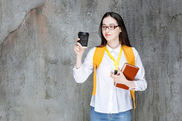 本とコーヒーを保持している眼鏡の女子学生。高品質の写真