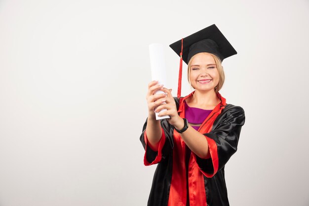 Female student in gown received diploma on white.