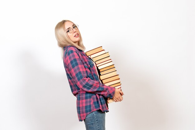 female student holding different heavy books on white