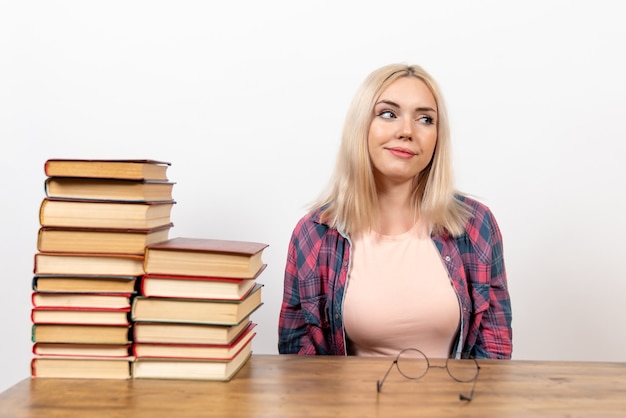 Foto gratuita studentessa appena seduta con libri su bianco chiaro