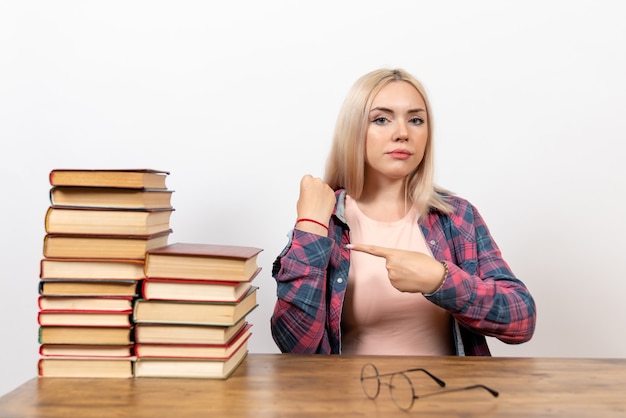 Foto gratuita studentessa appena seduta con i libri che punta al polso su bianco