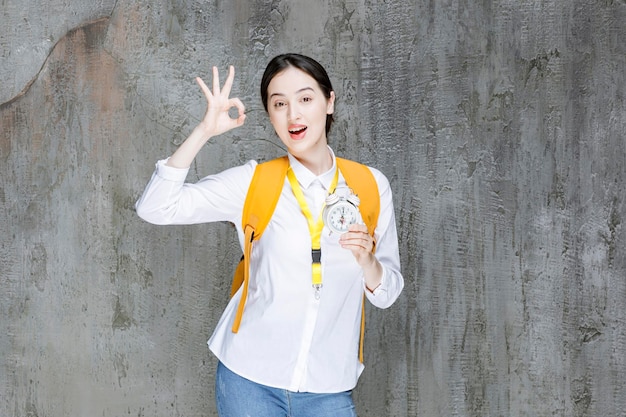 Female student with backpack holding clock. High quality photo