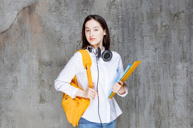 Female student with yellow backpack and headphones standing with book. High quality photo