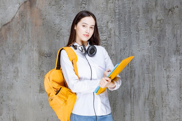 Female student with yellow backpack and headphones standing with book. High quality photo