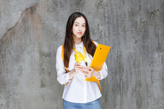 Female student with yellow backpack holding water bottle and folder. High quality photo