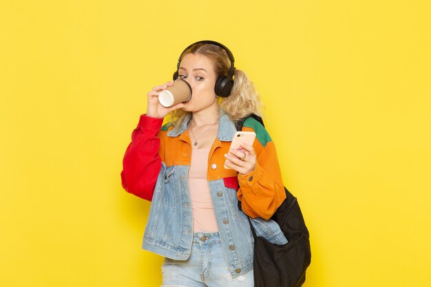 노란색에 전화를 사용하여 커피를 마시는 현대 옷에서 젊은 여성 학생