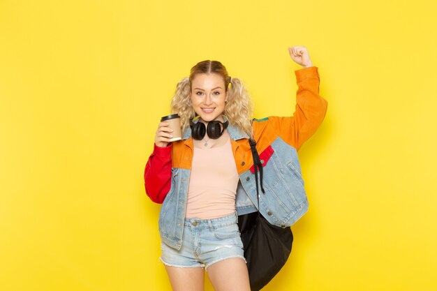 female student young in modern clothes holding coffee and flexing on yellow